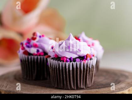 Drei Schokoladen-cupcakes zum valentinstag auf einer Holzplatte und im Hintergrund verschwommene Tulpen. Hellgrüner Hintergrund. Stockfoto