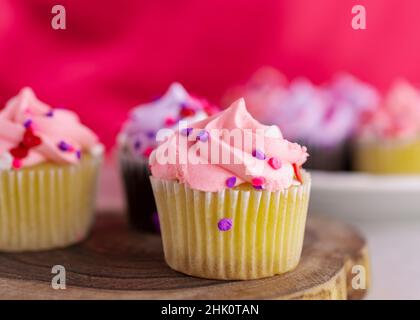 Eine Nahaufnahme einer Auswahl an kleinen Valentinstag-Cupcakes auf einer Holzplatte. Rosa Hintergrund mit einer sehr geringen Schärfentiefe. Zusätzliche c Stockfoto