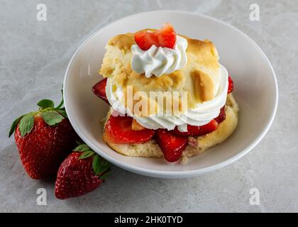 Draufsicht auf einen Erdbeer-Shortcake mit Schlagsahne. Zwei zusätzliche ganze Beeren auf der Seite der Schüssel. Stockfoto