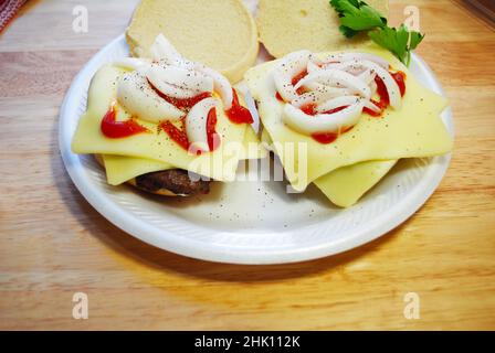 Zwei übereinander geteilte Cheeseburger mit Catsup und Zwiebeln in Scheiben Stockfoto