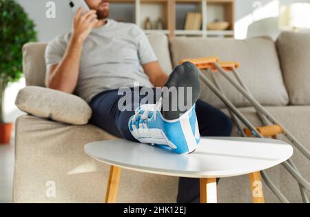 Verletzter Mann mit Beinverband spricht am Telefon Stockfoto