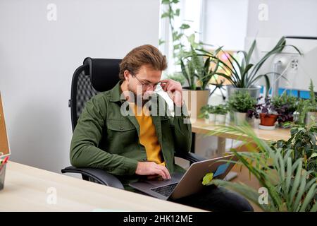 Konzentrierter ernsthafter Mann sitzt mit Laptop und denkt nach einem Brainstorming, arbeitet hart, im hellen Büro. manager Kerl mit Bart konzentriert auf die Arbeit. Bei der Arbeit Stockfoto