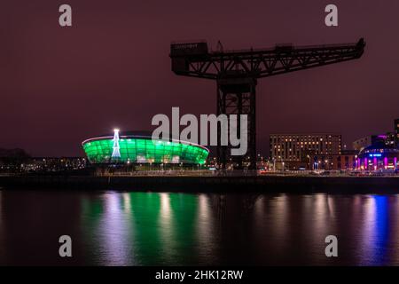 Der Finnieston Crane am Fluss Clyde mit der Hydro-Mehrzweck-Hallenarena, die im Hintergrund grün beleuchtet ist. Stockfoto