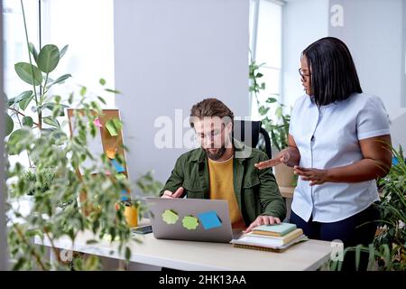 Schwarze Managerin Consulting Im Gespräch Mit Einer Mitarbeiterin Im Büro. Junge schwarze Dame Mentor Coach im Gespräch mit männlichen Kollegen Lehre Praktikant havin Stockfoto