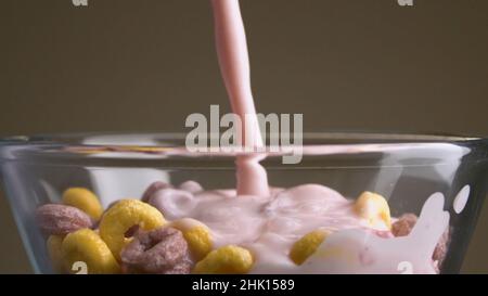 Flocken mit Milch. Archivmaterial. Nahaufnahme in mehrfarbigen süßen Flocken fügen Milch hinzu. Milch mit süßen bunten Ringen. Schädliche süße Lebensmittel. Stockfoto