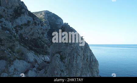 Herrliche Aussicht auf die Berghänge, die mit kleinen Bäumen und grünem Moos bedeckt sind, und große Klippen nahe dem Meer gegen den blauen Himmel. Wunderschöne Aussicht auf die Klippe Stockfoto