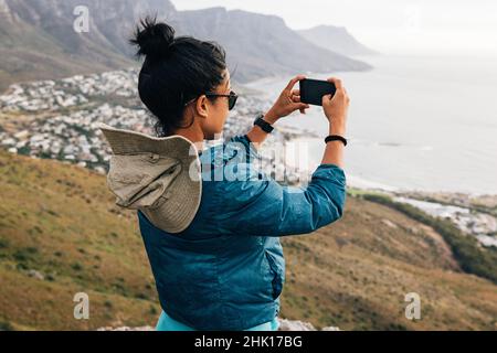 Junge Frau fotografiert mit ihrem Smartphone, während sie auf einem Berg wandert. Wandererin, die Fotos für ihre sozialen Medien macht. Stockfoto