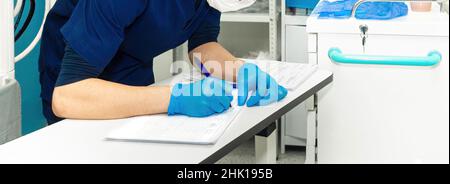 Ein Arzt in blauen sterilen Handschuhen schreibt in medizinischen Dokumenten. Selektiver Fokus. Panorama. Banner. Stockfoto