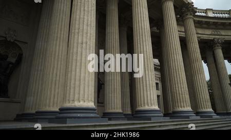 Untere Ansicht der antiken Säulen mit korinthischen Orden. Aktion. Starke Säulen auf dem Hintergrund des bewölkten Himmels. Altes Gebäude mit Portikus. Stockfoto