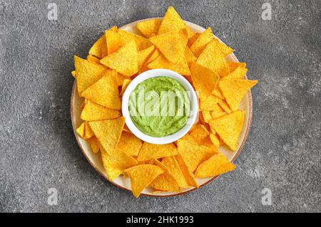 Mais-Tortilla-Chips in großen Teller mit Guacamole-Sauce auf grauem Hintergrund. Top-Evew. Stockfoto