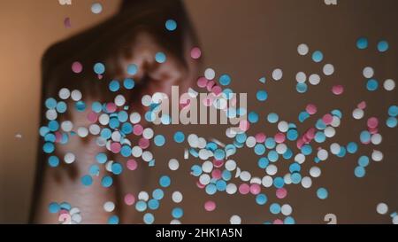 Frau Hände werfen rosa, weiß und blau rund geformten Konfetti auf flache transparente Oberfläche. Unterseite der weiblichen Hand, die kleine Kreise auf Glas setzt Stockfoto