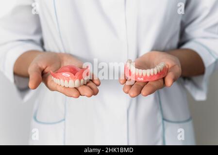 Der Zahnarzt hält Prothesen in den Händen. Zahnprothese in den Händen des Arztes Nahaufnahme. Vorderansicht der kompletten Prothese. Zahnmedizin Konzept Stockfoto