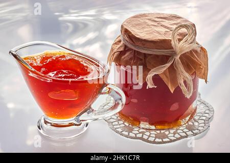 Obstmarmelade in einer Glasschüssel und Glas auf weißem, sonnigen Hintergrund Stockfoto