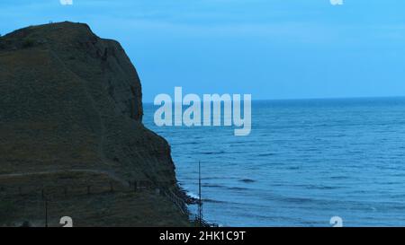 Luftaufnahme der großen grauen Klippe und der Meereswellen, die auf den Felsen gegen den blauen Abendhimmel brechen. Wunderschöne abendliche Meereslandschaft Stockfoto