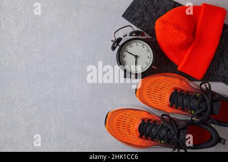 Orangefarbene Sneakers, orangefarbener Strickmütze, schwarze Leggings und Wecker Stockfoto