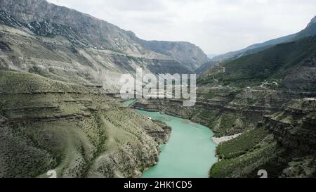 Luftaufnahme eines geschwungenen grünen Flusses, der zwischen Felshängen fließt. Aktion. Sommer Naturlandschaft mit einem malerischen Bach und Bergkette Stockfoto