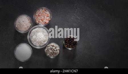 Verschiedene Arten von Salz und kulinarischen Gewürzen in Glasplatten auf dunklem Grund Stockfoto