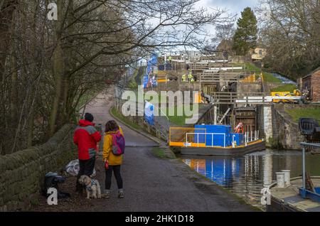Ein Paar mit einem Hund, der auf dem Kanalpfad bei Bingley steht. Sie beobachten Wartungsarbeiten an den Schleusentoren an fünf Schleusen. Stockfoto