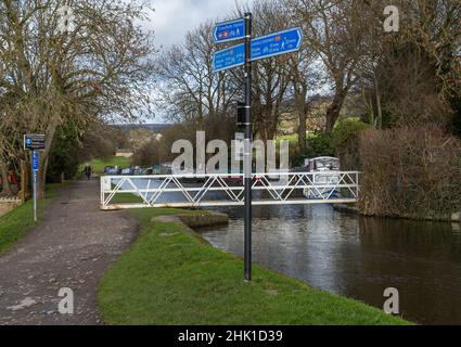 Der Leeds Liverpool Canal in Bingley, Yorkshire. Es gibt ein Schild am Kanal auf dem Schleppweg und eine Schaukelfußbrücke über den Kanal. Stockfoto