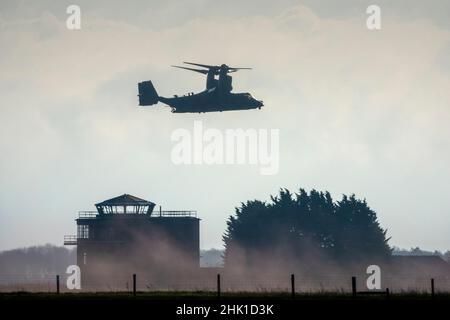 Eine teilweise abgeschottete Seitenaufnahme einer Bell Boeing V-22 Osprey, die über einem Flugfeldkontrollturm schwebt und lokalen Staub aufsaugt Stockfoto