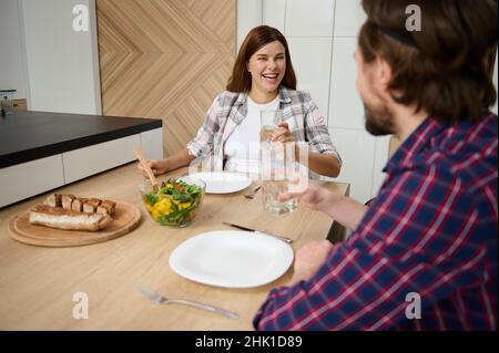 Der tägliche Lebensstil eines schönen jungen kaukasischen Paares, das gemeinsam zu Mittag essen, sich amüsieren und lachen kann, während es am Tisch in der sitzt Stockfoto