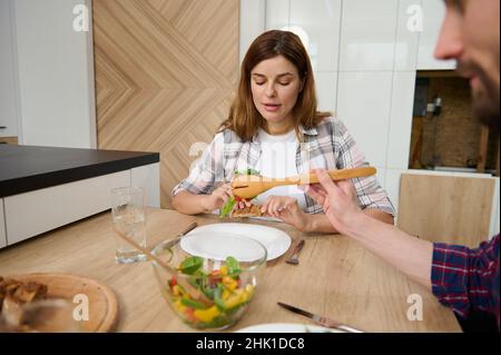 Tägliche Routine des glücklichen jungen kaukasischen Paares genießen Mittagessen zusammen, sitzen am Tisch in ihrer geräumigen Villa mit schönen hellen Innenraum Stockfoto