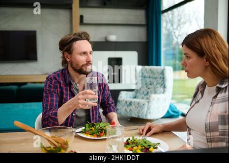 Gutaussehender kaukasischer Mann und Frau, Ehemann und Ehefrau, die zu Hause gemeinsam zu Mittag essen. Schönes Paar, das Spaß hat, zu Hause bei einem leckeren Mittagessen zu reden Stockfoto