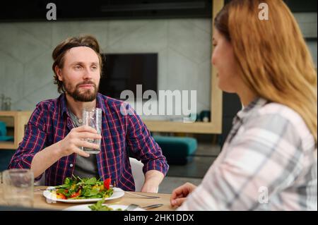 Gutaussehender europäischer Mann und Frau, Mann und Frau, die zu Hause gemeinsam zu Mittag essen. Schönes Paar, das Spaß hat, zu Hause bei einem leckeren Mittagessen zu reden Stockfoto