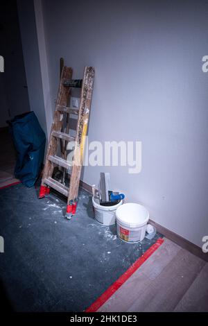 Eine hölzerne Stehleiter und ein Eimer Farbe stehen an der Wand in einem Flur Stockfoto