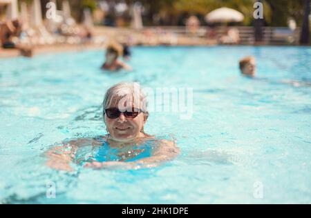 Ältere Frau mit grauen Haaren, in blauem Badeanzug, lächelnd im Hotelpool Stockfoto
