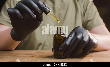 Hände tropfende CBD-Öltropfen in Glasflasche mit einer Pipette. Stockfoto