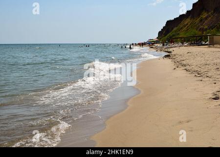 Schaumende Meereswellen Rollen am Sandstrand am Tag. Urlauber können in der Ferne Sonnenbaden und schwimmen Stockfoto