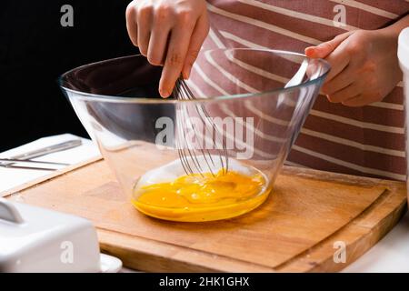 Nahaufnahme der Hände einer Frau, die Eier schlagen, um Teig auf dem Holztisch in der Küche zu machen. Hausgemachte Küche. Stockfoto
