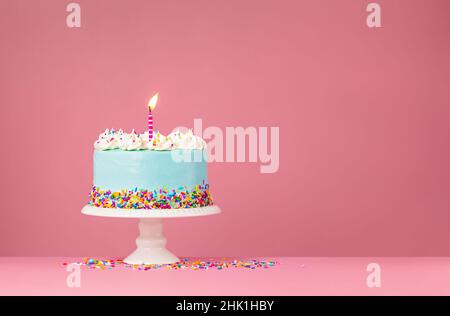 Blauer Geburtstagstorte mit bunten Streuseln und brennter Geburtstagskerze auf einem rosa Hintergrund. Stockfoto