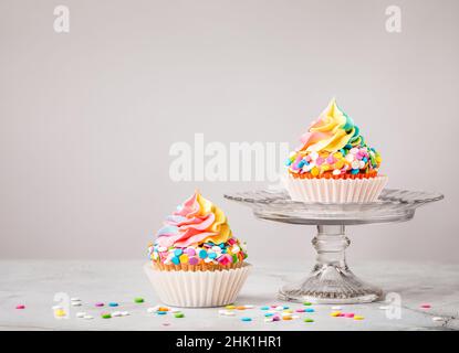 Zwei Rainbow Birthday Cupcakes mit bunten Streuseln auf hellgrauem Hintergrund. Stockfoto