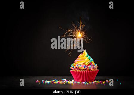 Rainbow Birthday Cupcake mit einem Glitzer und bunten Streuseln auf einem dunklen Hintergrund. Eine magische Geburtstagsfeier. Stockfoto