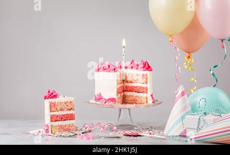 Pinkfarbene Funfetti-Geburtstagstorte mit Kerze, Geschenken, Hüten und bunten Luftballons auf hellgrauem Hintergrund. Szene von einer Geburtstagsparty! Stockfoto