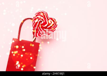 Rote Geschenktasche mit rotem Lollipop in Herzform auf rosa Hintergrund. Valentinstag Hintergrund. Liefer- und Einkaufskonzept. Draufsicht, Kopierbereich für t Stockfoto