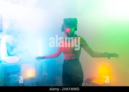Junge Frau mit Virtual-Reality-Brille im dunklen Raum mit Neonbeleuchtung. Wireless-Technologien. Stockfoto