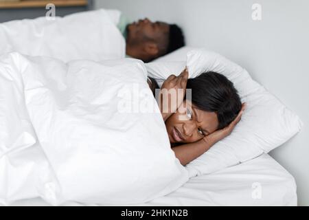 Depressive, traurige junge afroamerikanische Dame wacht vom Schnarchen und Lärm des schlafenden Mannes auf Stockfoto