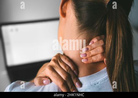 Junge Frau, die nach der Arbeit am pc an Nackenschmerzen litt und zur Schmerzlinderung den Hals massierte Stockfoto