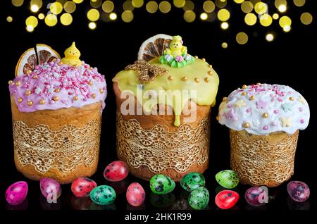 Verzierte Osterkuchen und bunte Wachteleier auf schwarzem, horizontalem Hintergrund mit goldenem Bokeh. Das Konzept des hellen Osterfestes Stockfoto