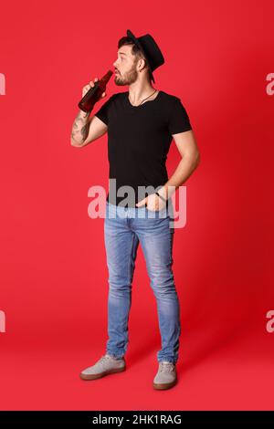 Stilvoller junger Mann, der Bier auf rotem Hintergrund trinkt Stockfoto
