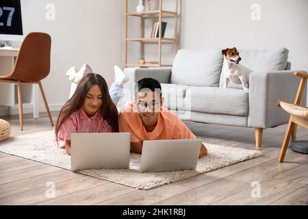 Junger Mann mit seiner Frau, der zu Hause Laptops auf dem Boden benutzt Stockfoto