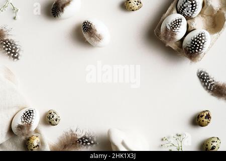 Ostereier im Minimalstil, verziert mit Federn, Hasen, Gypsophila-Blättern auf weißem Tisch. Frohe Ostern Grußkarte Vorlage. Stockfoto