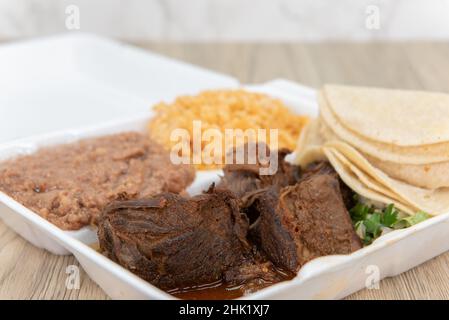 Herzhafte Bestellung von Birria-Eintopf, serviert zur Herstellung von Tacos mit den im Lieferumfang enthaltenen Tortillas, Reis und Bohnen in der Styroporbox. Stockfoto