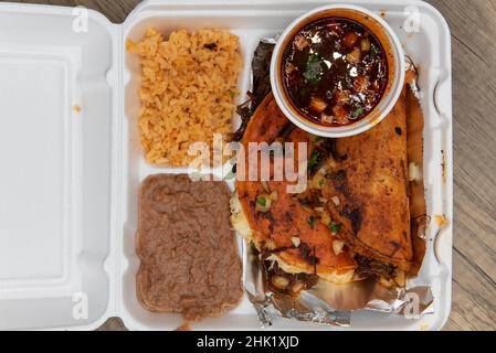 Blick von oben auf die Bestellung von Birria-Tacos, die in der Styropor-Box mit Reis und Bohnen perfekt frittiert wurden. Stockfoto