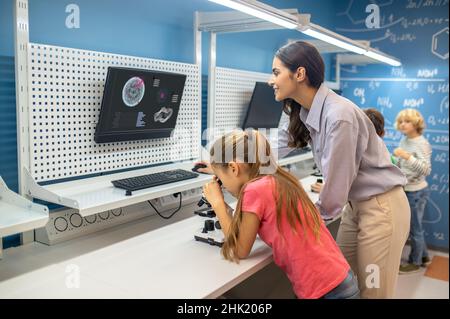 Frau, die auf das Ladeboard schaut, und Mädchen in der Nähe des Mikroskops Stockfoto