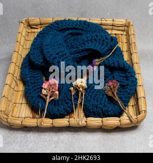 Nahaufnahme eines Strickschals aus Wolle und getrocknete Blumen in einem kleinen Korb aus Naturfasern Stockfoto