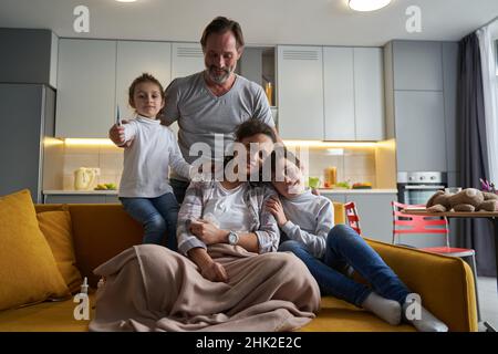 Kind mit Thermometer sitzt neben ihrer kranken Mutter Stockfoto